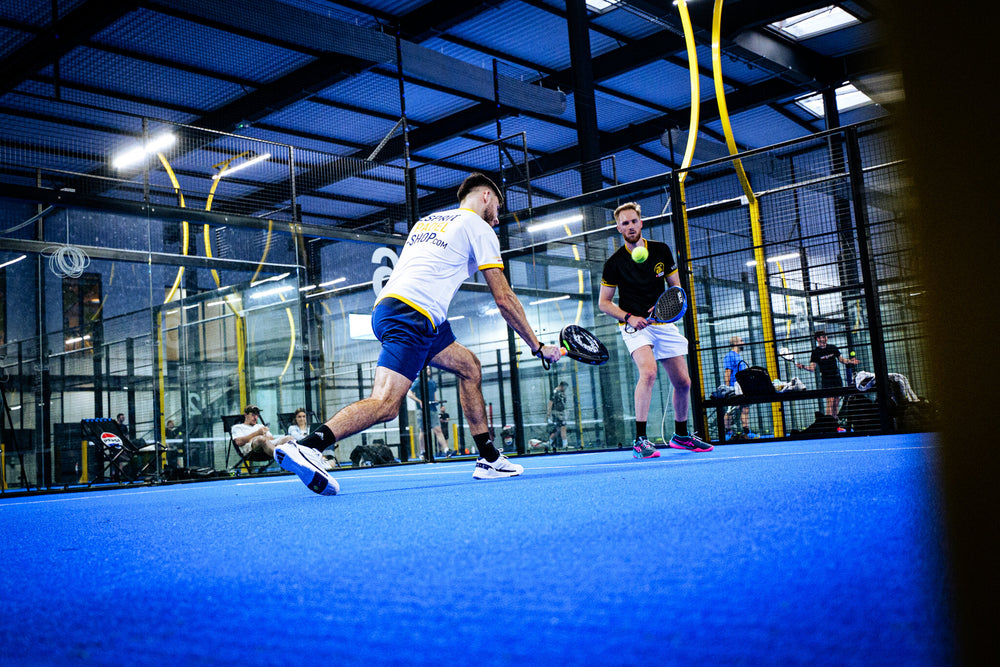 Deux joueurs en plein match de padel sur un terrain couvert, raquette en main